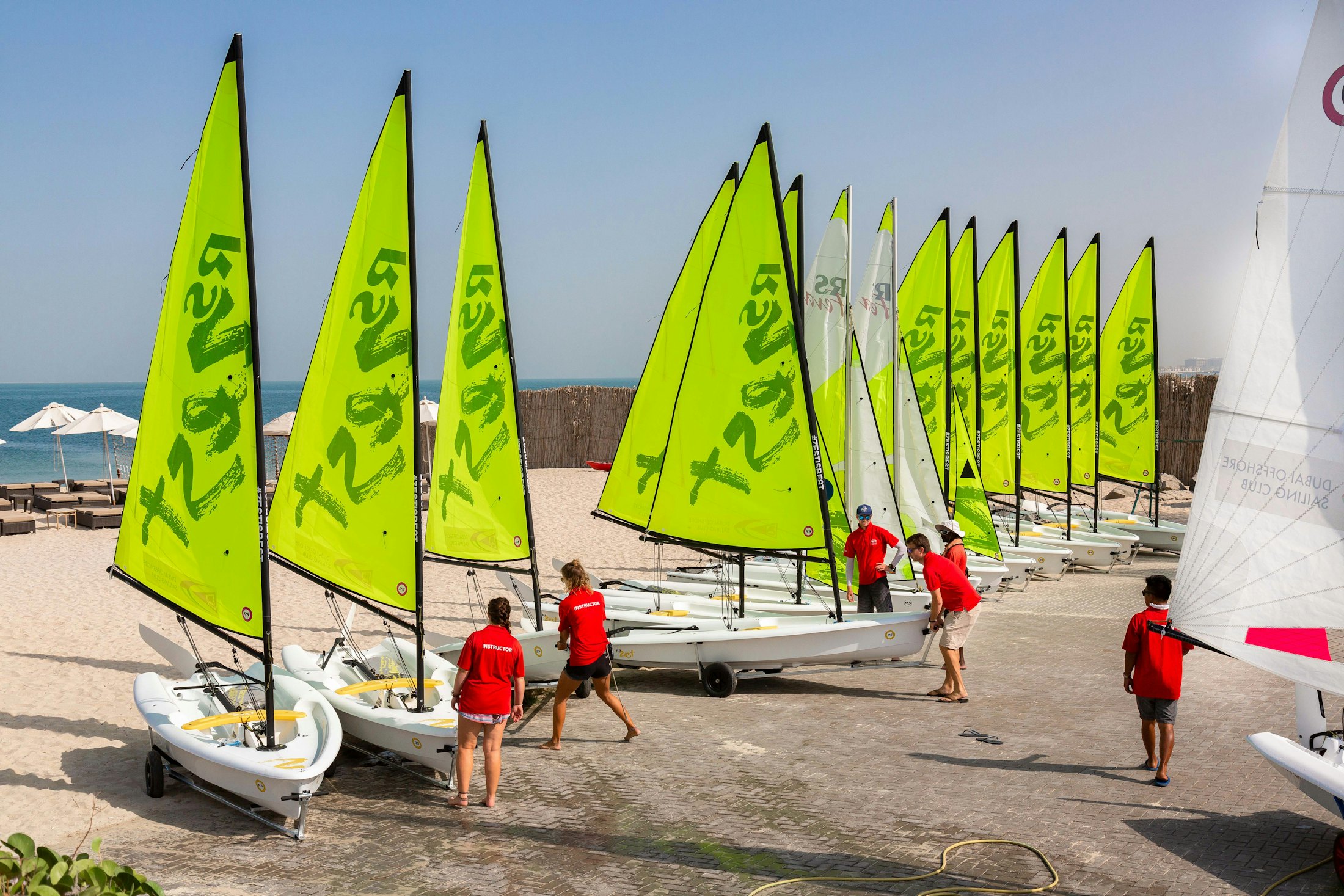 Dinghies rigged on a beach with club members preparing to launch.